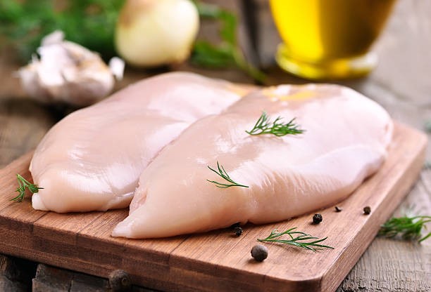Two pieces of skinless and washed chicken breasts neatly placed on a cutting board